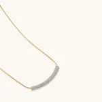 Gold-plated curved necklace, hoop earrings, and adjustable ring with pavé cubic zirconia stones on cream background.