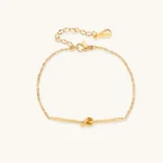 Delicate gold chain bracelet with minimalist bar and centered knot detail on cream background