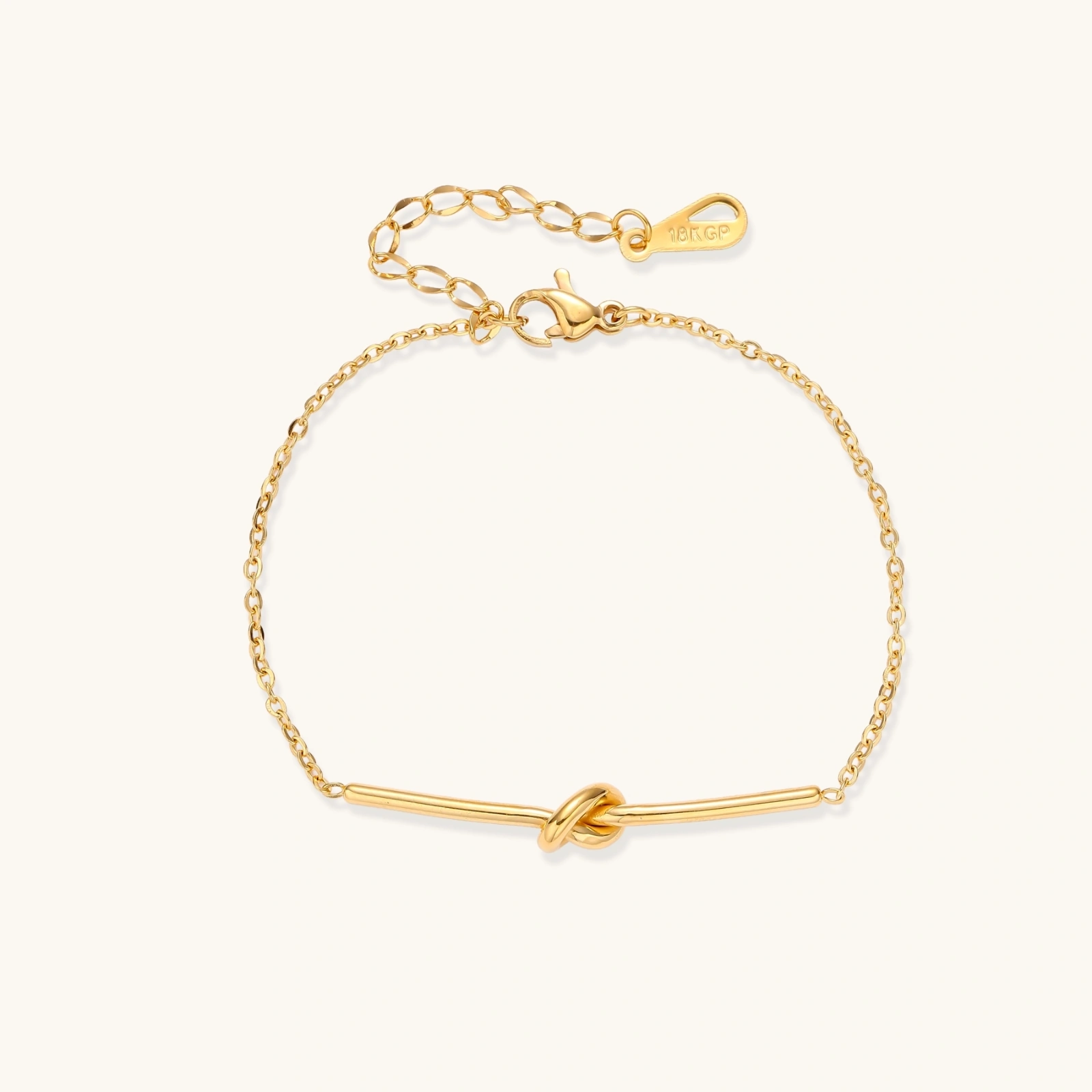 242426758369333248.webp Delicate gold chain bracelet with minimalist bar and centered knot detail on cream background