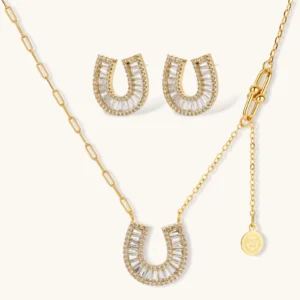 Gold-plated horseshoe necklace and earring set with baguette and round crystals arranged in geometric pattern on white background.