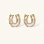 Gold-plated horseshoe necklace and earring set with baguette and round crystals arranged in geometric pattern on white background.