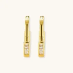 Close-up of gold-plated sterling silver huggie hoop earrings featuring rectangular cubic zirconia stones on neutral background.