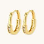 Close-up of gold-plated sterling silver huggie hoop earrings featuring rectangular cubic zirconia stones on neutral background.