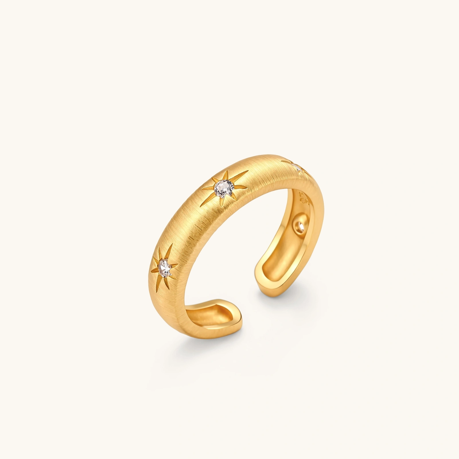 313699909507891200.webp Gold open-band cuff ring with brushed matte finish, engraved 8-point star motifs, and round CZ stones on white background.
